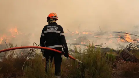A firefighter holds a hose as he looks at burning vegetation