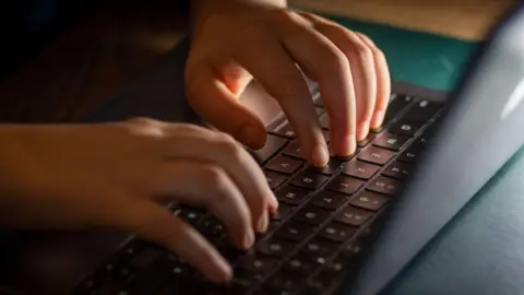 A close-up of a child's hands as they type on a black laptop.