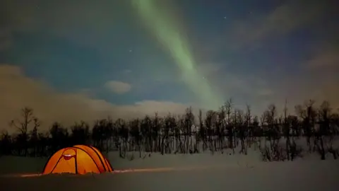 Sam Cox Tent glowing in the snow with the Northern Lights on display