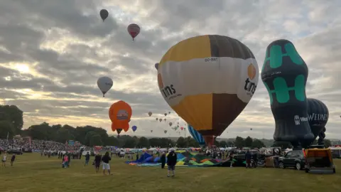 Hot air balloons are being prepared to take off, with some already ascending.