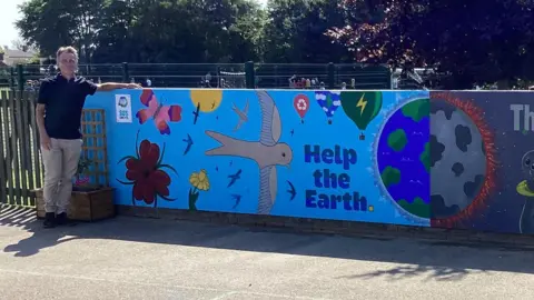 Federation of Fairfield and Colneis Artist Simon Oxley in front of the artwork