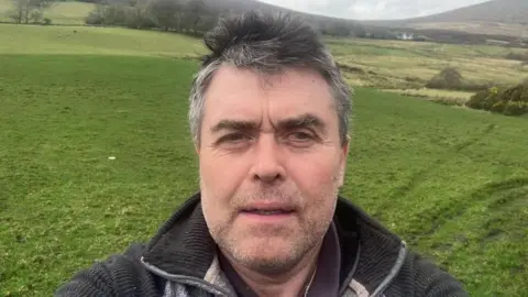 Thomas Conway Shows a man with grey hair and a dark 