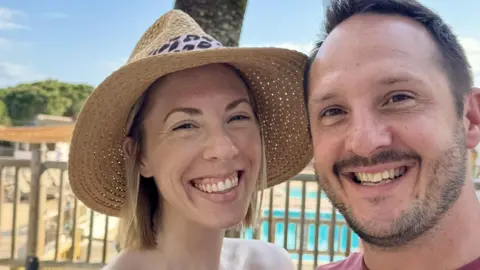 Daisy Woods Daisy Woods with her husband. She is wearing a straw hat and smiling in front of a pool. She has blonde shoulder-length hair. Her husband has brown hair and a light stubble. 