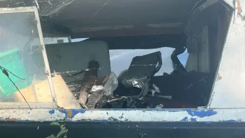 A seemingly abandoned boat. The photo is a close-up shot through a broken window showing a mess.
