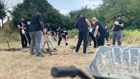 Emma Baugh/BBC Group of volunteers in black t-shirts digging in a field