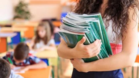A teacher holds school books while children work in a classroom