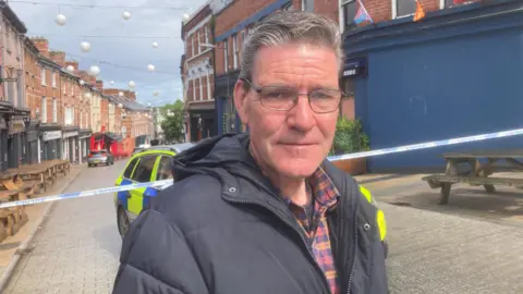 SDLP councillor John Boyle stands in front of the police cordon where a woman died after a fire in a flat in Londonderry