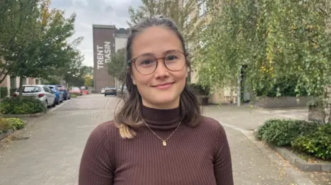 Dahlia Panova stood on a road in Trent Basin, with a block of flats behind her showing the words "Trent Basin" on the wall.