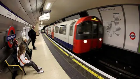 Getty Images A platform at Knightsbridge Tube station, with a Tube train pulling up to the platform. A few people are waiting on the platform, some sitting on a bench.