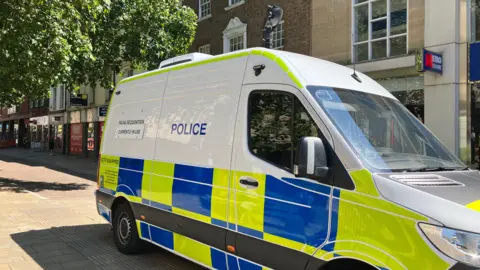 Shariqua Ahmed/BBC A white police van - with green and blue checks on it and black cameras on the roof.