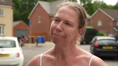 Claire Tootill is wearing a white top and standing in a street, with houses and cars in the background.