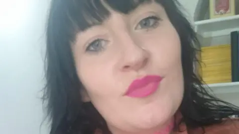 Selfie of Lisa-Marie Hopkins. She has dyed black hair with a fringe, grey eyes and bright pink lipstick.