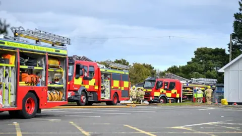 Pacemaker Three Northern Ireland Fire and Rescue Service vehicles in red and yellow at Whiteabbey Hospital, with staff nearby.