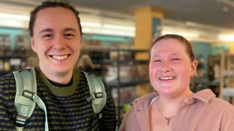 Matthew Simpson, wearing a green and black jumper and with a backpack's straps on his shoulders, and Daisy Clelland in a pink jacket