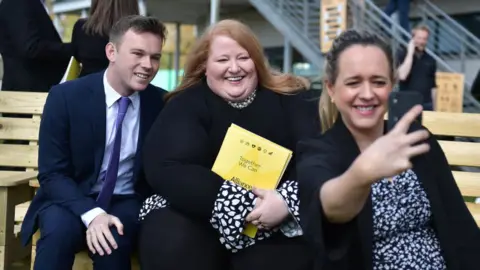 Getty Images Kate Nicholl (R) takes a selfie photograph of Alliance party leader Naomi Long (C) and fellow party candidates following the Alliance party manifesto launch at CIYMS recreational grounds on April 27, 2022 in Belfast.