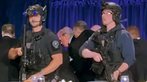 Armed guards surround Donald Trump as agents escort him out off the hotel stage.