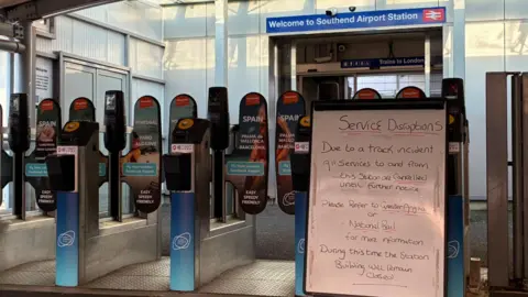 Matt Knight/BBC A whiteboard in front of closed railway gates. It says there has been an incident and all services are cancelled until further notice.
