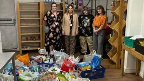 Merseyside Police Four women stand in a room behind a large number of filled shopping bags on the floor.