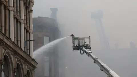PA Media A high-reach appliance spraying water on the remains of the building. 