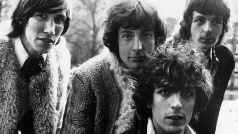 Getty A black and white image showing a close-up of the members of the band Pink Floyd (from left to right: Roger Waters, Nick Mason, Syd Barrett and Richard Wright) pictured in 1967. Roger Waters, Nick Mason and Richard Wright are standing behind Syd Barrett. They are outside and trees can just be seen behind them. 