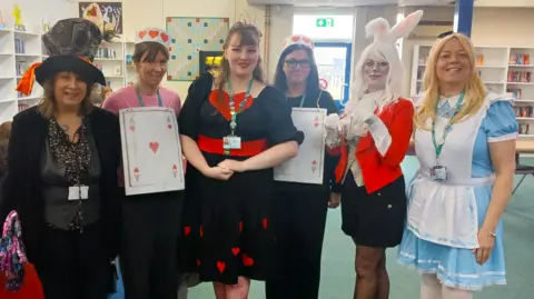 SBL Academy Six staff members at Sir Bernard Lovell Academy dressed as the characters from Alice's Adventures in Wonderland. There is the Mad Hatter, playing cards, the Queen of Hearts, the White Rabbit, and Alice. 