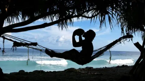 Bob Lisale drinks coconut milk as he watches the king tides pound the coast of Funafuti Atoll, 19 February 2004, home to nearly half of Tuvalu's entire population of 11,500