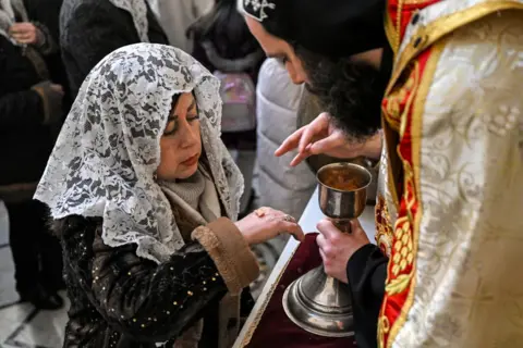 Getty Images Seorang umat menerima komuni selama kebaktian Natal di Gereja Apostolik Armenia Mar Sarkis (St Sargis) di Bab Sharqi di kota tua Damaskus pada 6 Januari 2025.