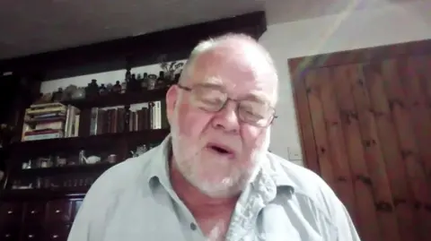 Dr David Hillebrandt. He has short grey hair and a short grey beard, and is wearing glasses. 
