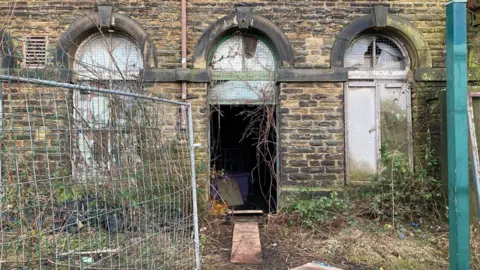 Charles Heslett/BBC A metal fence which has been pushed to one side leaving a walkway into a downstairs section of the mill. 