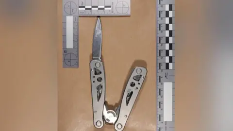 PA Media The multi-tool knife used by the teenager, pictured alongside a ruler along the top and bottom. The blade is protruding out of the silver metal case.