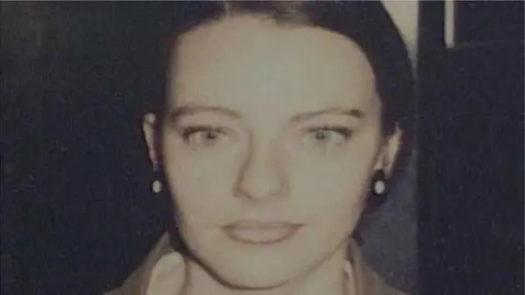 Tracey Wylde has dark hair scraped back and large black and white earrings. She is looking into the camera. 