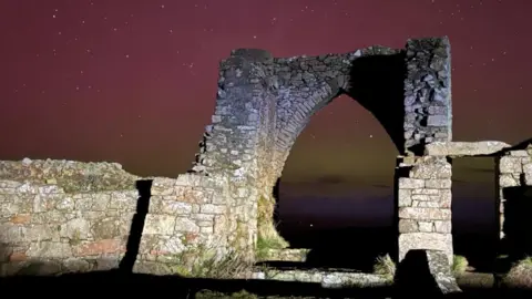 ROBERT HALL Ruins of a castle with the northern lights in the background. The stars are also very visible in the sky
