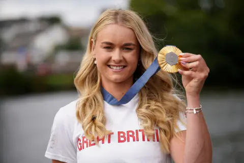 Hannah Scott holds her medall up to the camera. She wears her Team GB t shirt
