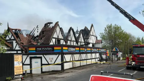 Richard Daniel/BBC A nightclub, pictured in the middle of the day, with a roof that has been destroyed in a fire. A fire engine is parked opposite the venue. There is a long aerial ladder rising into the sky above the building. Some smoke can be seen billowing out of the venue.