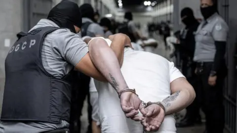 A Salvadoran police officer escorts an alleged member of the Tren de Aragua in Tecoluca, El Salvador