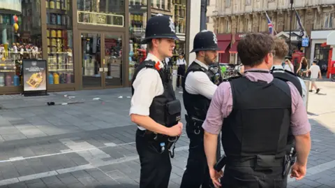 Two uniformed police officers speak to two plainclothes police officers at the crime scene cordon in Leicester Square