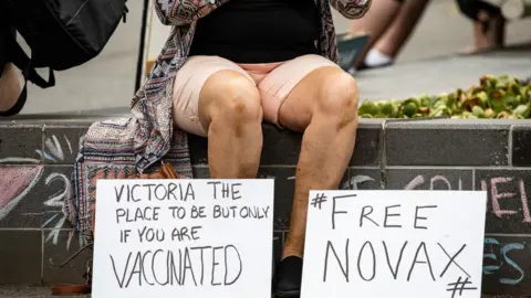 Getty Images Novak Djokovic supporter displays anti-vaccination signage as they gather outside Park Hotel where Djokovic was taken pending his removal from the country after his visa was cancelled by the Australian Border Force on January 06, 2022 in Melbourne, Australia.