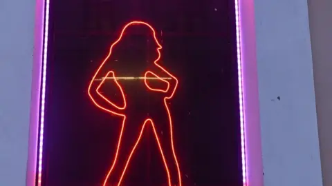 A red neon light in the silhouette of a woman with her hands on her hips