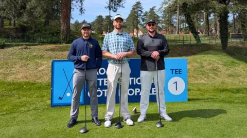 Matt Crawley Three men standing with golf clubs on a putting green. 