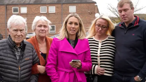 Shaun Whitmore/BBC The family stand in front of a court building. Sarah Lenton, who is wearing a bright pink coat, stands with a mobile phone in her hand.