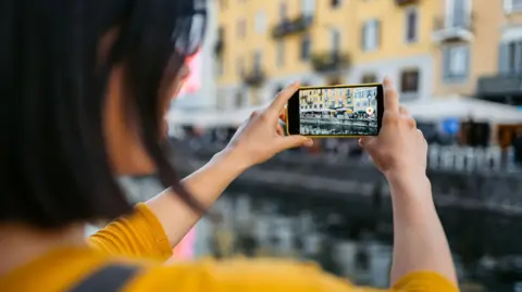 Getty Images A woman holds her phone in front of her so she can film a canal in Milan