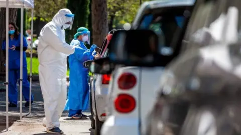 Getty Images Medical workers perform swabs as drivers line up at a drive-through testing facility for COVID-19 in Rome