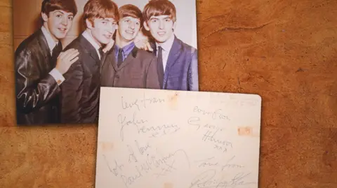 Dawsons On the top right is a picture of the four Beatles in the mid-1960s. On the bottom right is a piece of paper signed "with love" by all four.