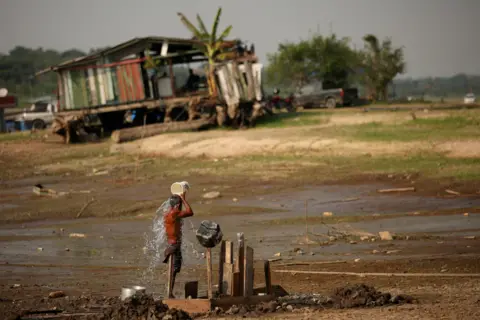 Reuters Fisherman Raimundo da Silva do Carmo, 67, baths with water from a well on Puraquequara Lake, which has been affected by drought, in Manaus, Brazil, October 6, 2023.