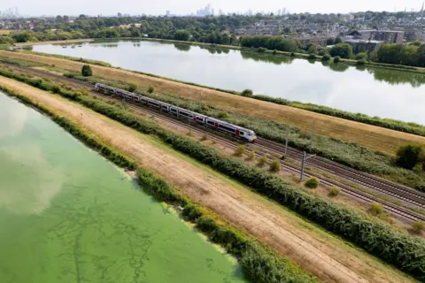 EPA An aerial view taken with a drone shows low water levels at the Walthamstow Wetlands, with green algae on water to left of the train track which has another body of water beyond it