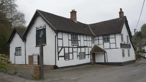 The George and Dragon pub in Erlestoke, near Devizes. It is white with a brown roof and sits just on the road with a small pavement. 