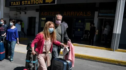 Getty Images Tourists pull their suitcases as they leave the international airport of Heraklion upon their arrival to spend their holidays on the island of Crete on May 14, 2021