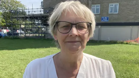Councillor Janine Howarth standing in front of a council house tower block surrounded by scaffolding.