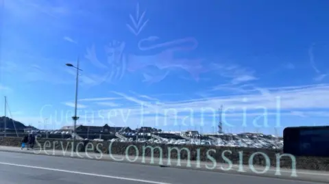 A reflection of a road and harbour full of boats in a window. The window has translucent logo of the Guernsey Financial Services Commission with a red lion.