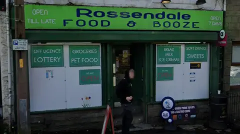 Google Street view image of Rossendale Food & Booze, a shop with a green sign and boarded up windows advertising food and groceries